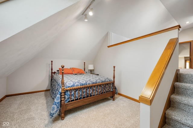 carpeted bedroom featuring vaulted ceiling, rail lighting, and baseboards