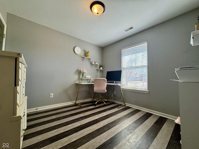 unfurnished office featuring visible vents, baseboards, wood finished floors, and a textured wall