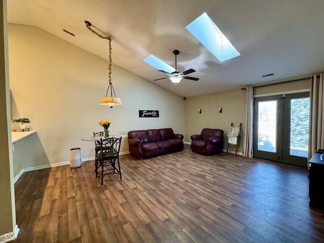 living room featuring visible vents, a ceiling fan, vaulted ceiling with skylight, baseboards, and dark wood-style flooring