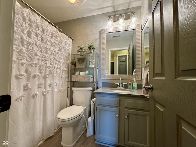 bathroom with vanity, wood finished floors, visible vents, toilet, and a textured wall