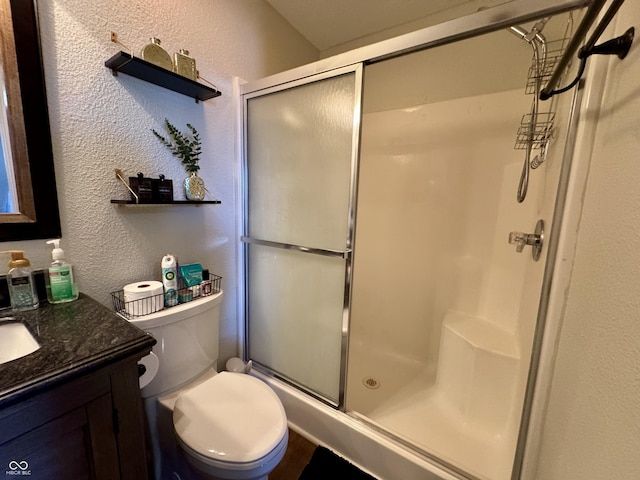 bathroom with a stall shower, toilet, vanity, and a textured wall