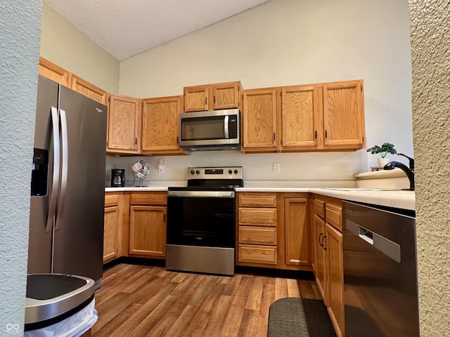 kitchen featuring light wood-style flooring, a sink, stainless steel appliances, light countertops, and vaulted ceiling