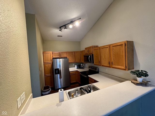 kitchen with a textured ceiling, stainless steel appliances, light countertops, vaulted ceiling, and a textured wall