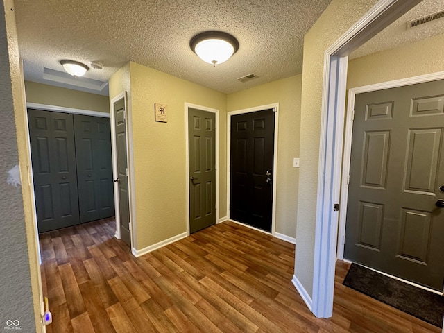 entrance foyer featuring dark wood-style floors, visible vents, and a textured wall