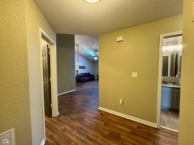 hallway featuring a sink, baseboards, dark wood-style flooring, and a textured wall