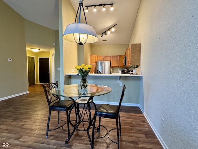 dining area featuring high vaulted ceiling, track lighting, baseboards, dark wood-style flooring, and a textured wall