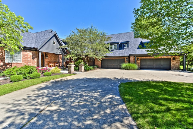 view of front of house with a shingled roof, a front yard, concrete driveway, and brick siding