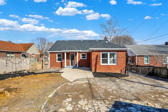 back of house with brick siding, a shingled roof, a chimney, and fence