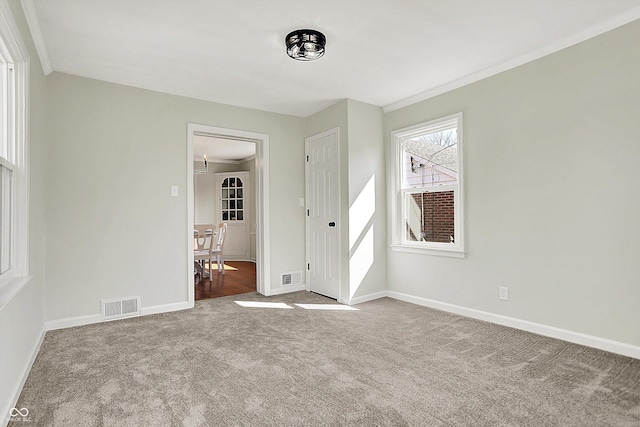 carpeted empty room featuring crown molding, baseboards, and visible vents