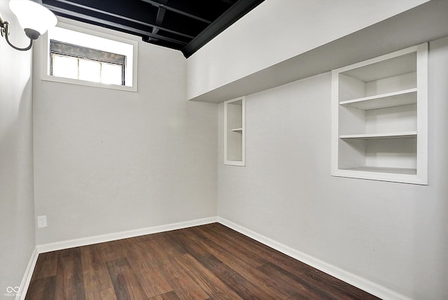 below grade area with built in shelves, baseboards, and dark wood-style floors