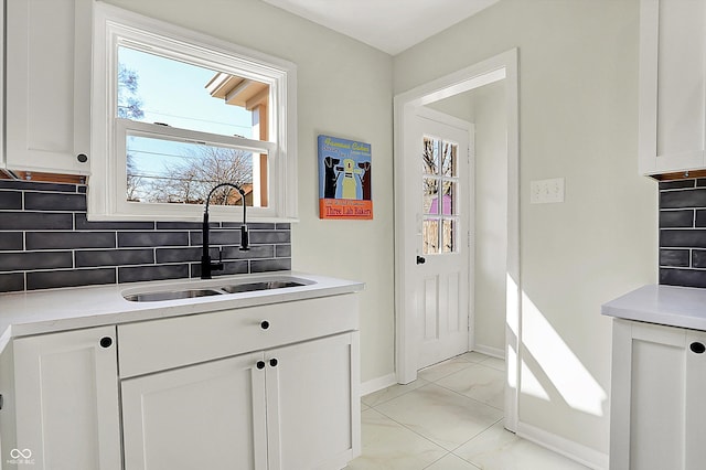 kitchen with decorative backsplash, light countertops, white cabinetry, and a sink