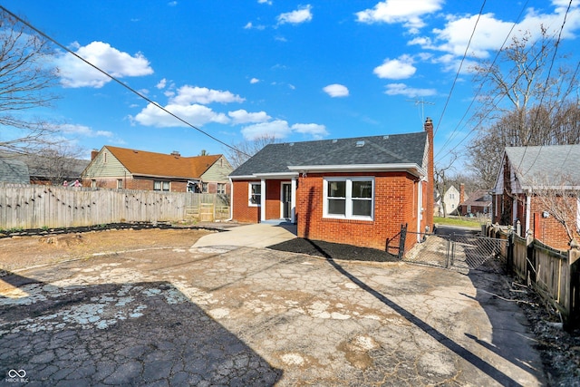 rear view of property with a gate, fence, a shingled roof, a chimney, and brick siding