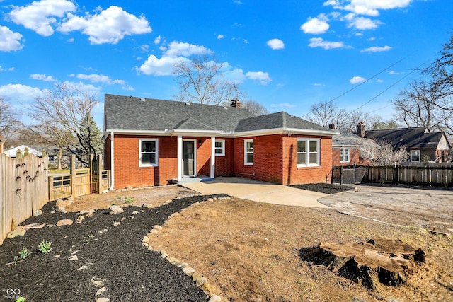 rear view of property with a patio, brick siding, roof with shingles, and a fenced backyard