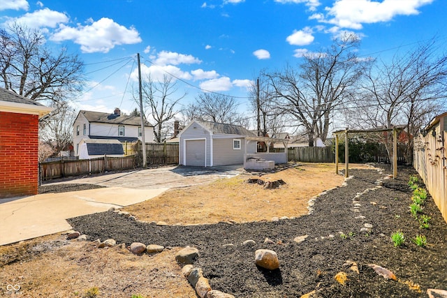 view of yard with an outbuilding, a detached garage, a fenced backyard, concrete driveway, and a patio area