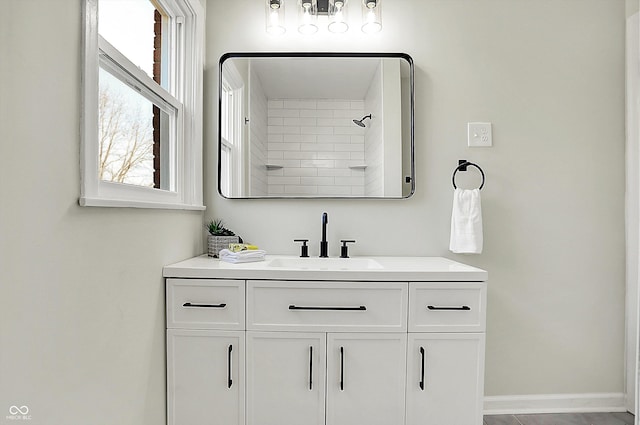 bathroom featuring tiled shower, vanity, and baseboards