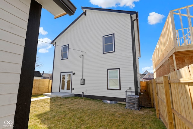 back of house featuring french doors, central air condition unit, a lawn, and a fenced backyard