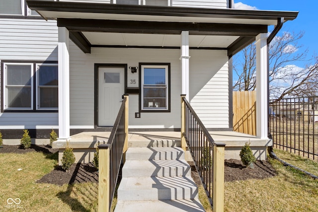 view of exterior entry featuring fence and covered porch