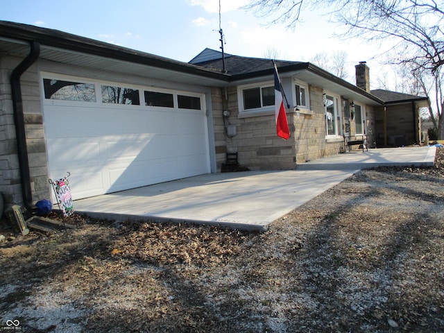 view of home's exterior featuring an attached garage, stone siding, driveway, and a chimney