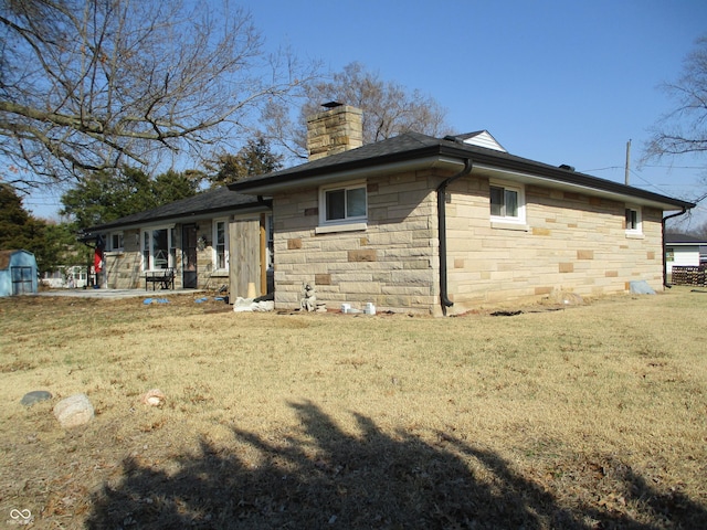 rear view of property featuring a yard, stone siding, and a chimney