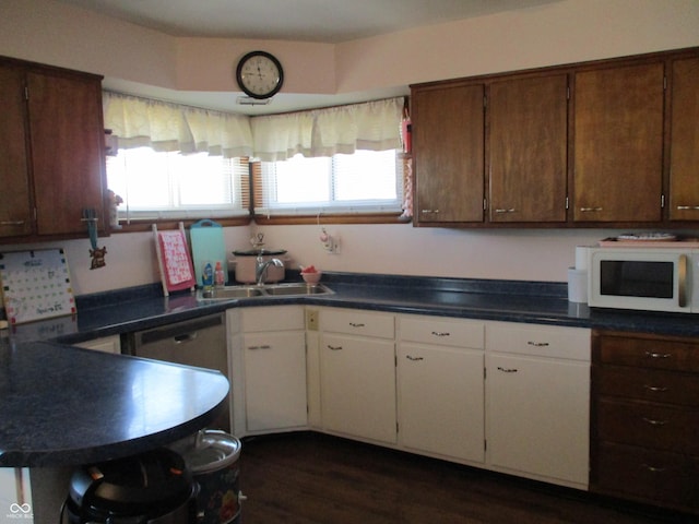 kitchen featuring a sink, white microwave, dark countertops, and white cabinets