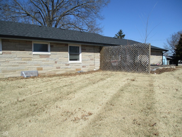 view of home's exterior featuring stone siding, a lawn, and roof with shingles