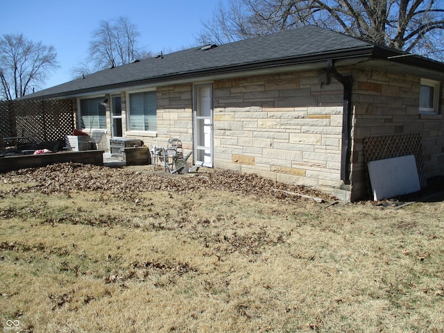 back of house with stone siding and a shingled roof