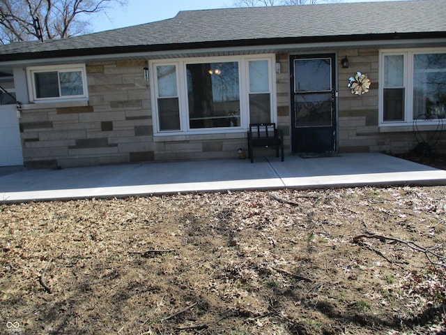 back of house with a patio area, stone siding, and a shingled roof