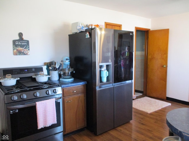 kitchen featuring dark wood-style floors, brown cabinetry, stainless steel appliances, and dark countertops