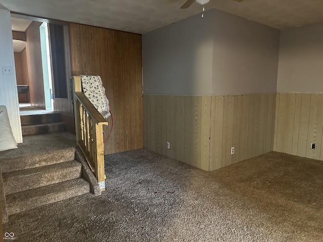 interior space with a wainscoted wall, ceiling fan, wooden walls, and carpet floors