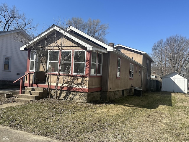 view of front facade with an outdoor structure, central air condition unit, a front yard, and a shed