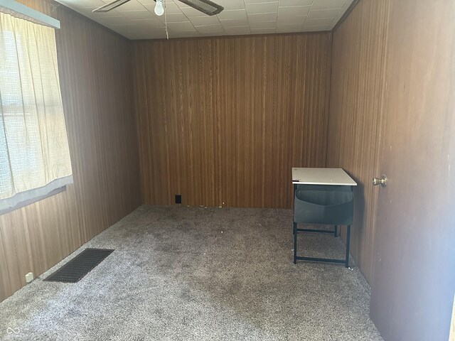 unfurnished room with carpet flooring, visible vents, and wood walls