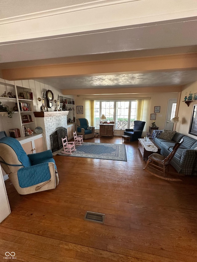 living area featuring visible vents, beam ceiling, wood finished floors, and a fireplace