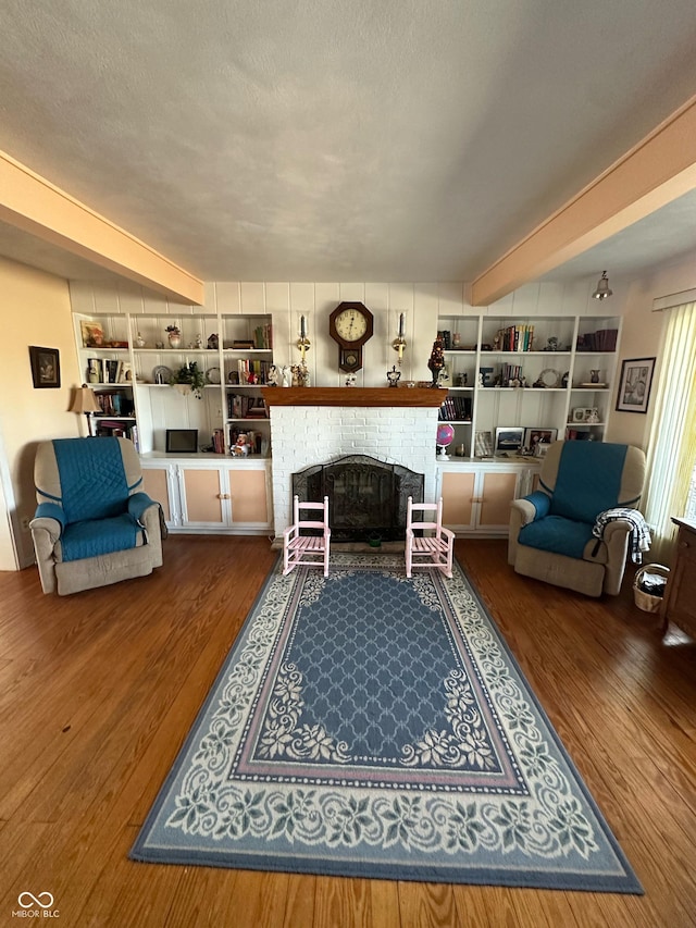 living area featuring beam ceiling, a brick fireplace, a textured ceiling, and wood finished floors