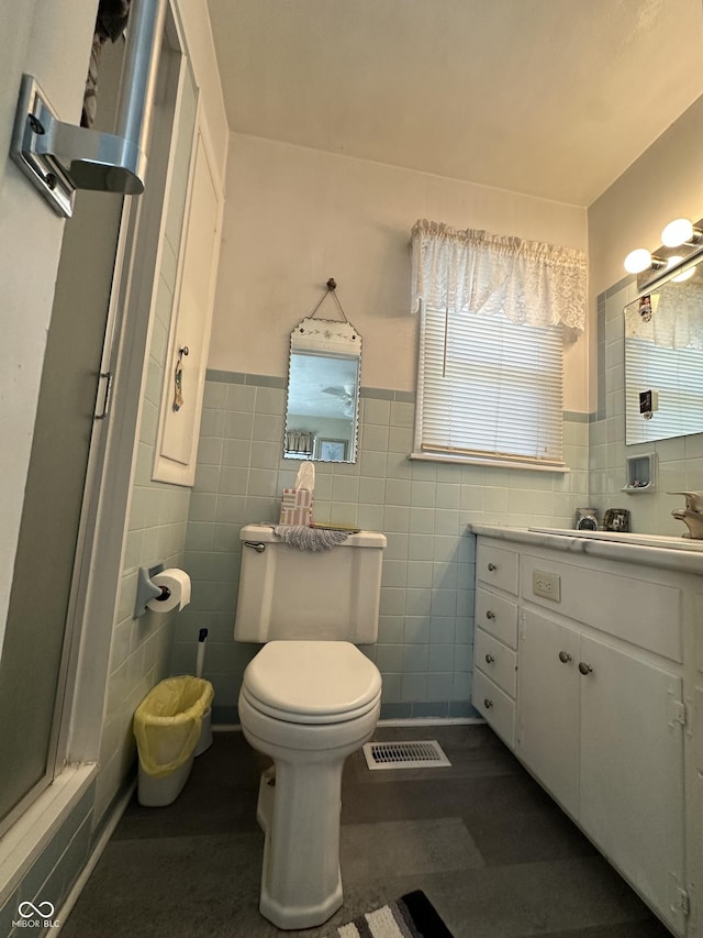 full bath with a shower with door, visible vents, tile walls, toilet, and vanity