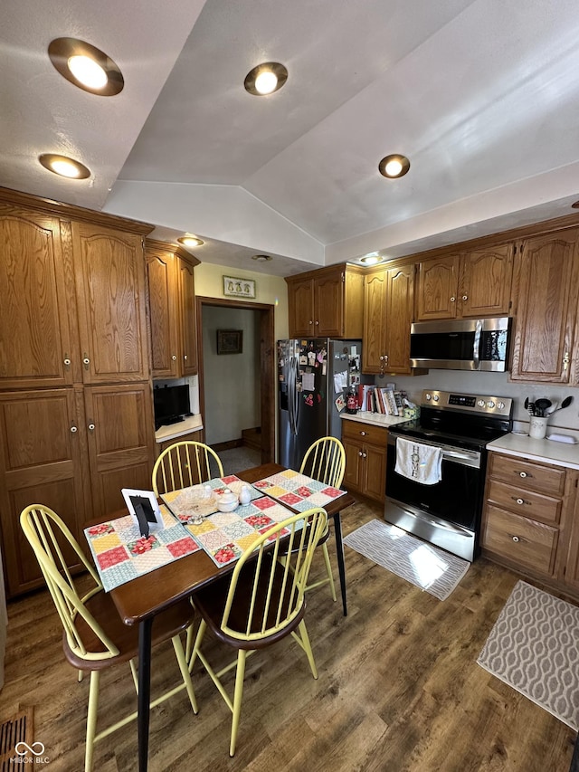 kitchen with dark wood-type flooring, light countertops, lofted ceiling, brown cabinets, and appliances with stainless steel finishes