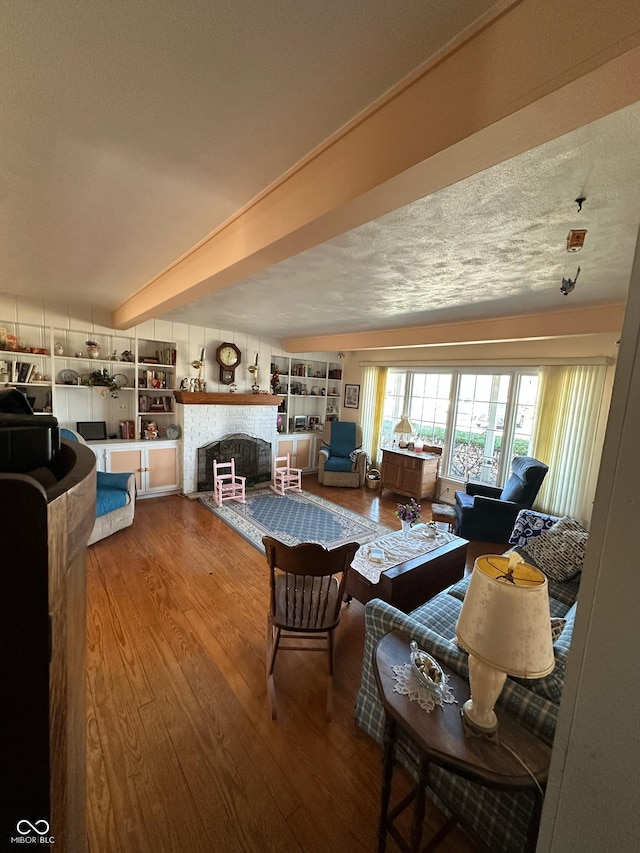 living area featuring beam ceiling, a fireplace with flush hearth, a textured ceiling, and wood finished floors