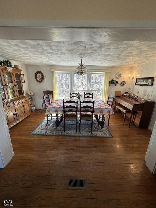 dining space with visible vents, a textured ceiling, dark wood finished floors, and a decorative wall