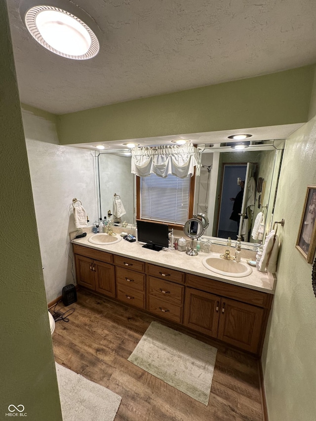 bathroom featuring a sink, a textured ceiling, wood finished floors, and double vanity