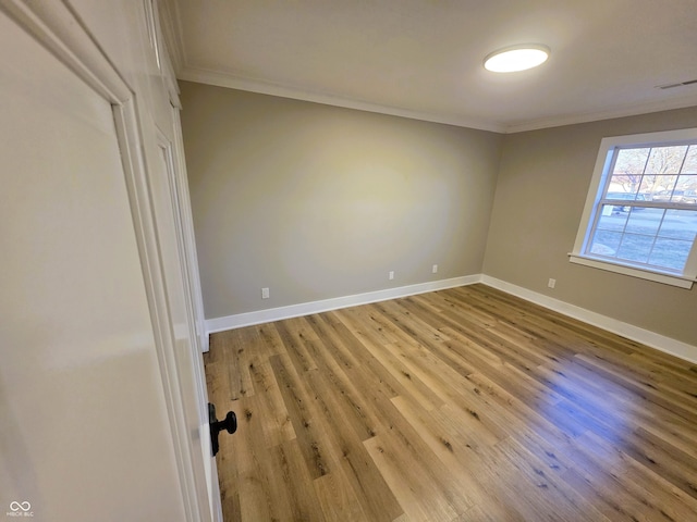 spare room featuring light wood finished floors, visible vents, baseboards, and ornamental molding