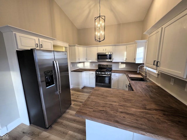 kitchen with high vaulted ceiling, a sink, appliances with stainless steel finishes, white cabinetry, and dark countertops