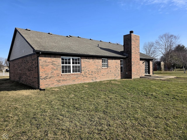 rear view of house with brick siding, a chimney, a lawn, and roof with shingles