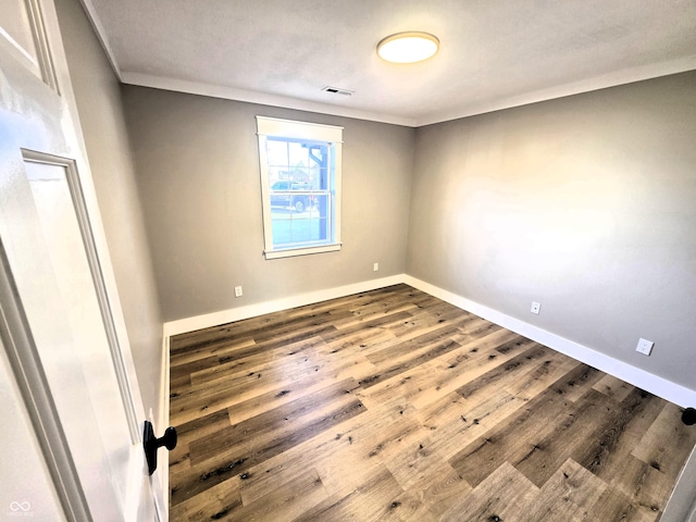 empty room featuring visible vents, baseboards, wood finished floors, and ornamental molding