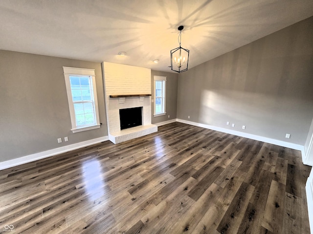 unfurnished living room featuring a brick fireplace, baseboards, an inviting chandelier, and dark wood-style floors