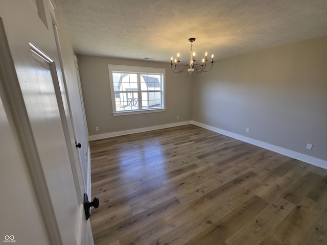 spare room with a notable chandelier, a textured ceiling, baseboards, and wood finished floors