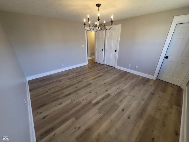 empty room with a chandelier, visible vents, baseboards, and wood finished floors