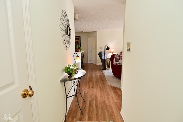 corridor with light wood-style floors, baseboards, and a textured ceiling