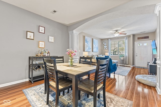 dining room with wood finished floors, visible vents, baseboards, decorative columns, and ceiling fan