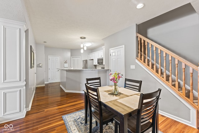 dining room with stairs, wood finished floors, baseboards, and a textured ceiling