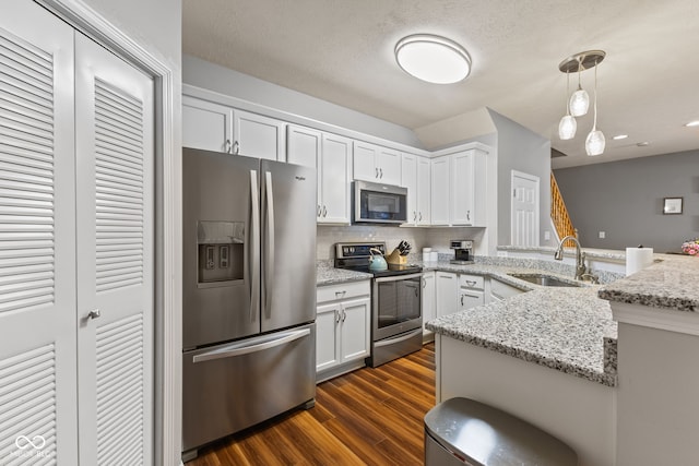 kitchen featuring dark wood finished floors, a peninsula, a sink, stainless steel appliances, and white cabinets