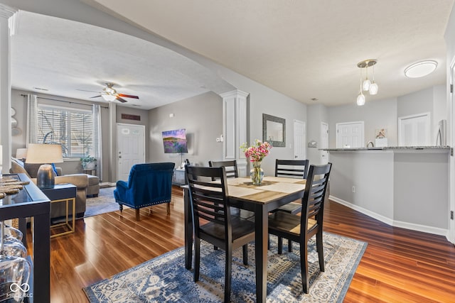 dining area featuring a ceiling fan, decorative columns, wood finished floors, and baseboards